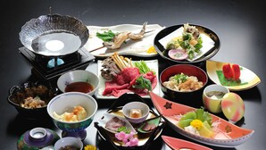 On peut voir une variété d’assiettes et de bols sur une table, notamment une théière, une assiette avec de la viande et un bol contenant une fleur.