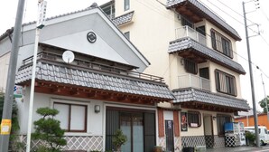 Il s’agit d’un bâtiment traditionnel japonais, doté d’un toit recouvert de tuiles, de balcons en bois et d’un petit jardin agrémenté de plantes en pot.