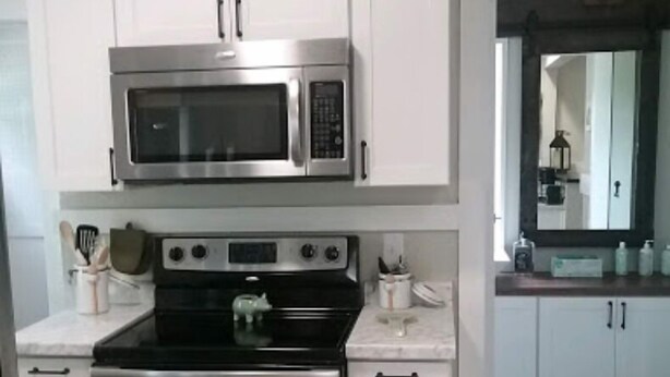 A kitchen with white cabinets, a stainless steel microwave, and an oven.