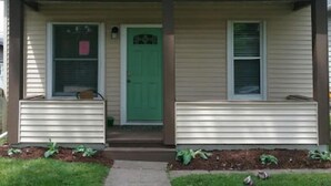 A two-story house with a green front door, a covered porch, and a small front yard.