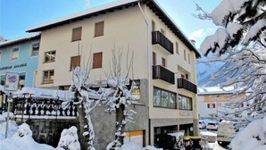 A multi-story building with a flat roof and balconies, surrounded by snow-covered trees and a clear sky.