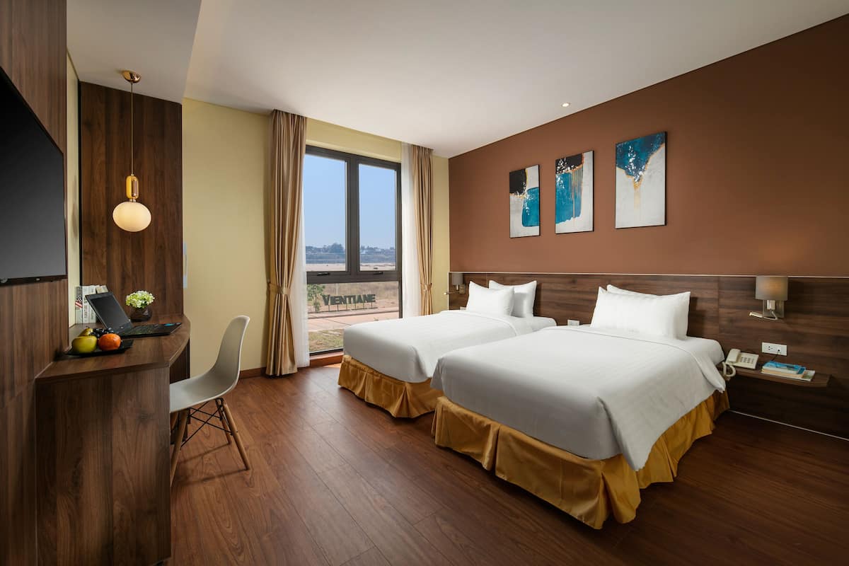 Une chambre d’hôtel avec deux lits, un bureau avec un ordinateur portable, une chaise et une vue sur l’extérieur.
