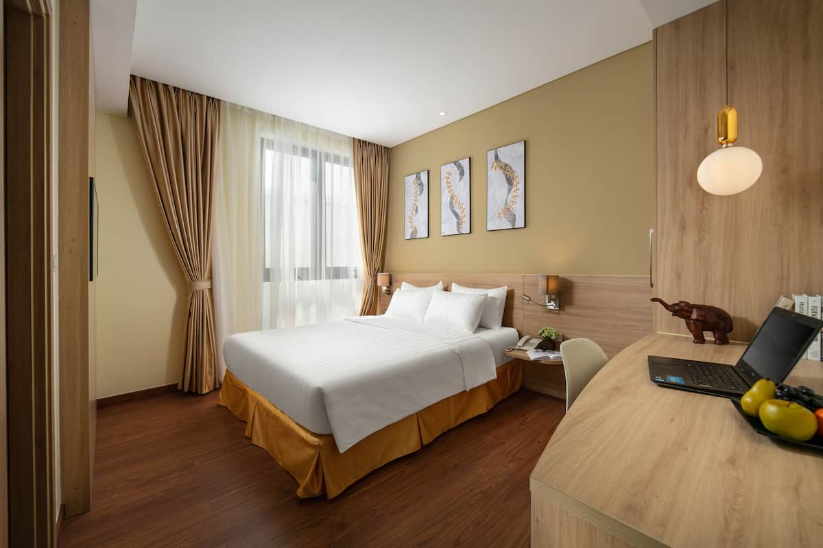 Une chambre d’hôtel avec un grand lit, un bureau avec un ordinateur portable et un panier de fruits.