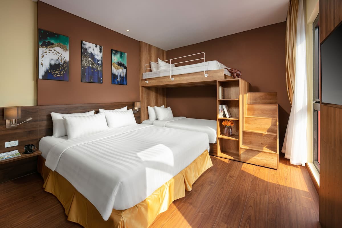 Une chambre d’hôtel avec un lit superposé, une tête de lit en bois, une table de chevet avec une lampe et des œuvres d’art murales.