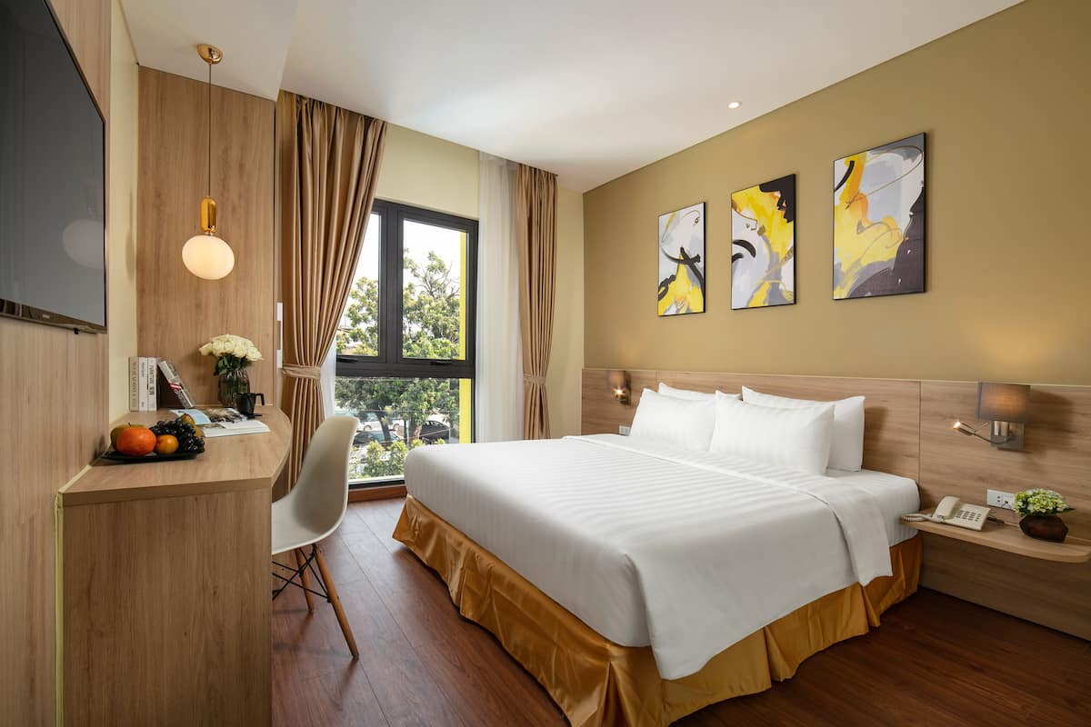 Une chambre d’hôtel avec un lit, un bureau, une chaise, des œuvres d’art et une fenêtre avec des rideaux.