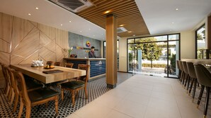 A modern hotel lobby with a reception desk, wooden chairs, a dining area with a patterned floor, and large windows offering a view of the outdoors. - Viryla Boutique Hotel (Vientiane)
