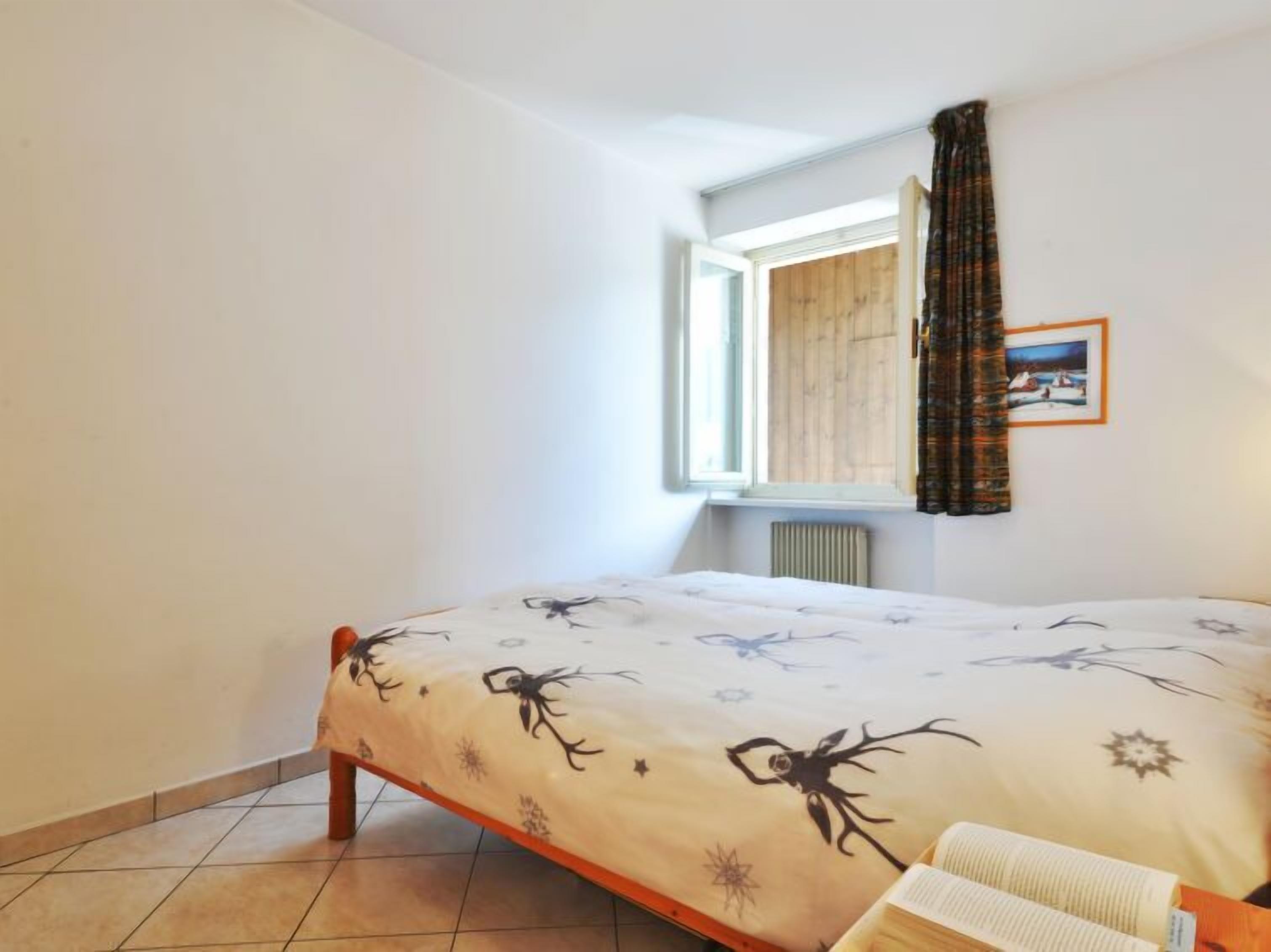 Un dormitorio con cama, ventana con cortinas, radiador y un cuadro en la pared.