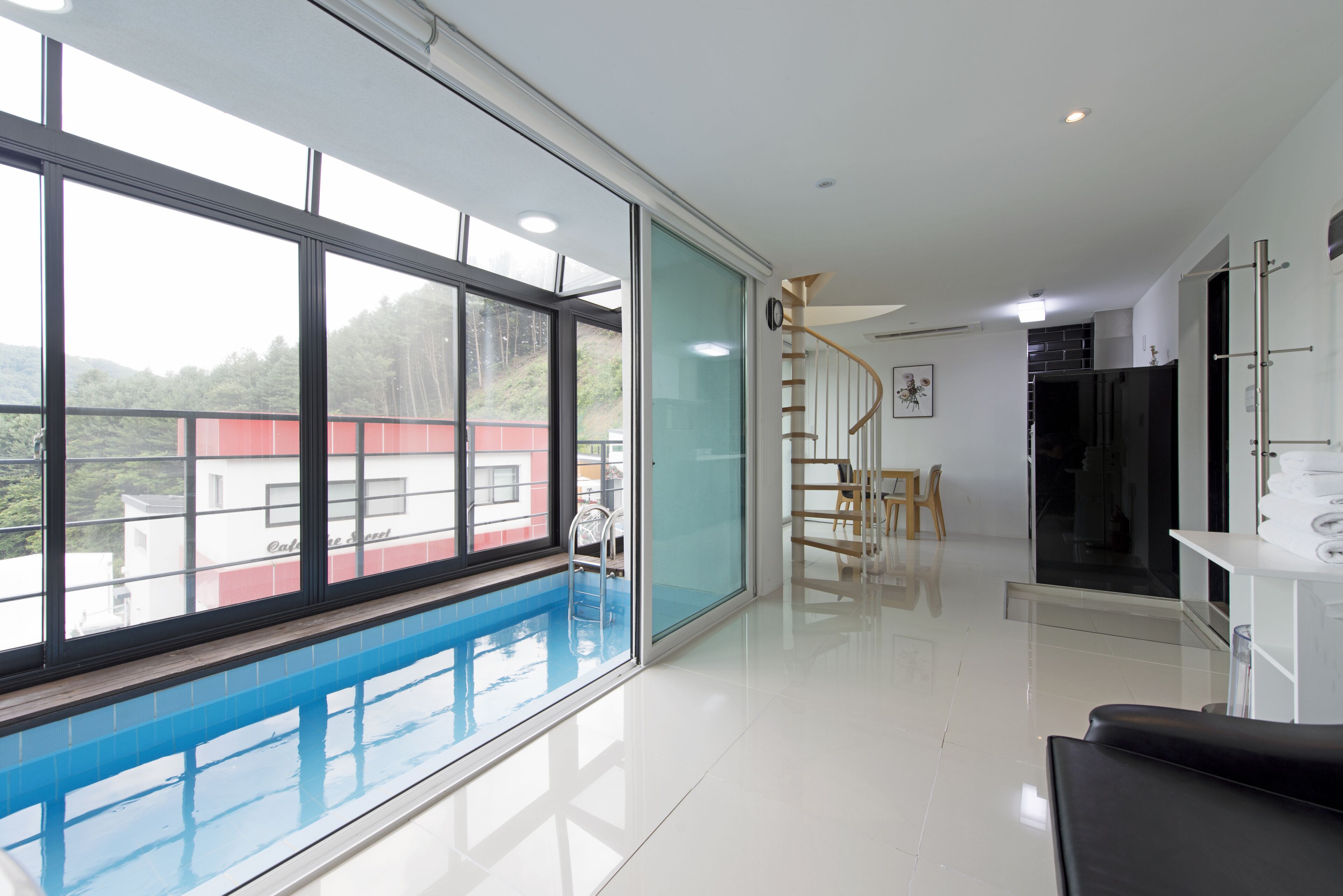 A modern interior with a large window, a pool, a staircase, and a kitchen area.