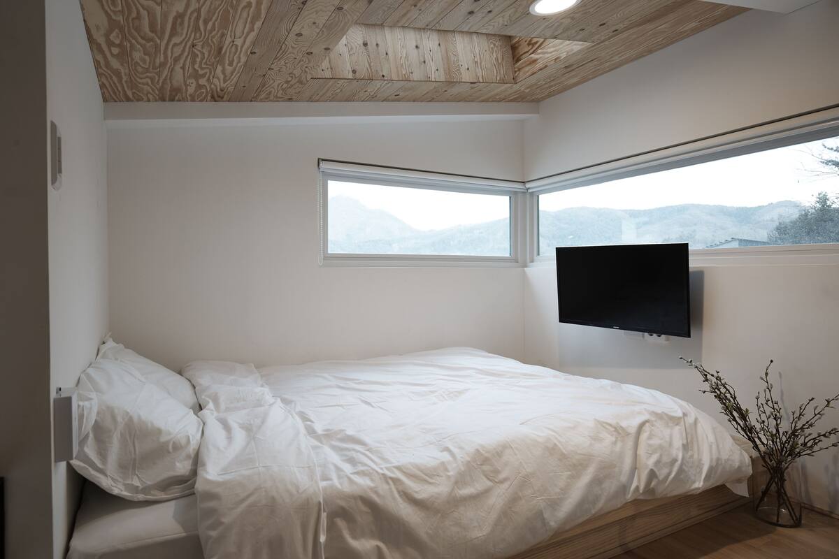 Une chambre à coucher avec un lit, une fenêtre, un téléviseur à écran plat et une vue sur les montagnes.