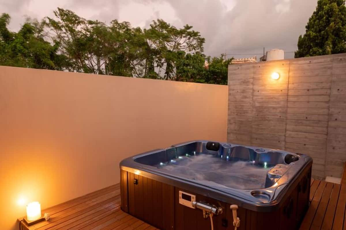 A hot tub on a wooden deck with a wall and trees in the background.