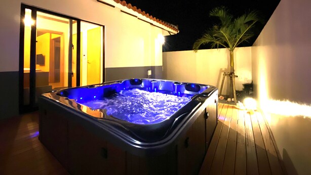 A hot tub on a wooden deck with a palm tree and a building in the background. - SUMU Villa (Nago)
