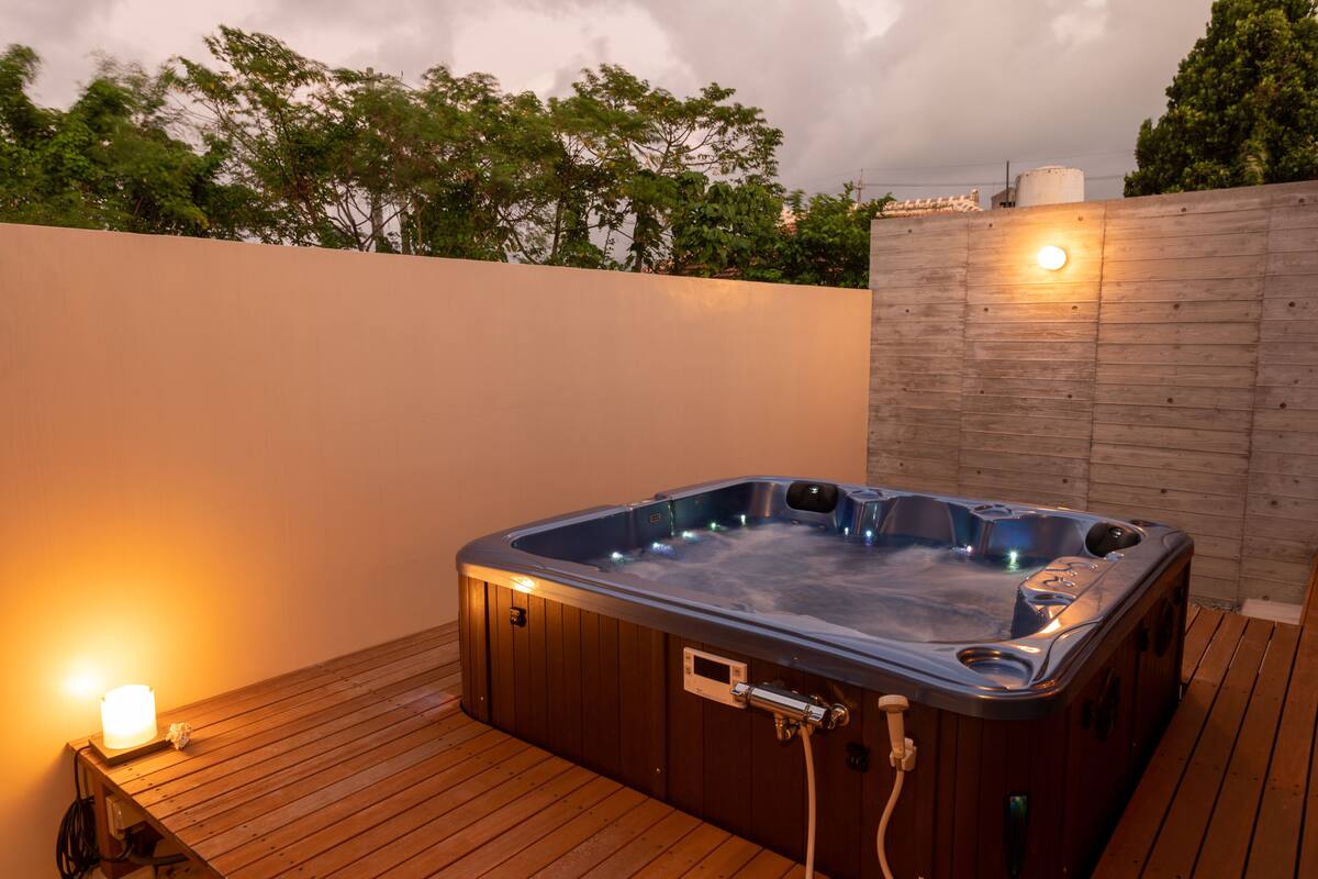 A hot tub on a wooden deck with a wall and trees in the background.