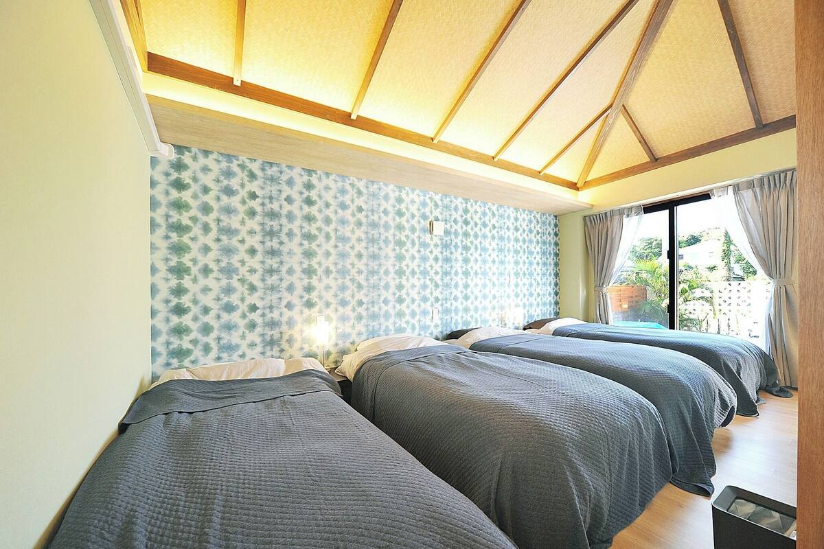 A room with three beds, a patterned wall, and a window with curtains.