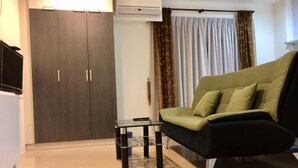Uma sala de estar moderna com um sofá verde, uma mesa de vidro pequena e um guarda-roupa com duas portas.