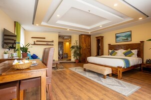 Una habitación de hotel con una cama de madera, un escritorio con una cesta, una silla y un ventanal grande.