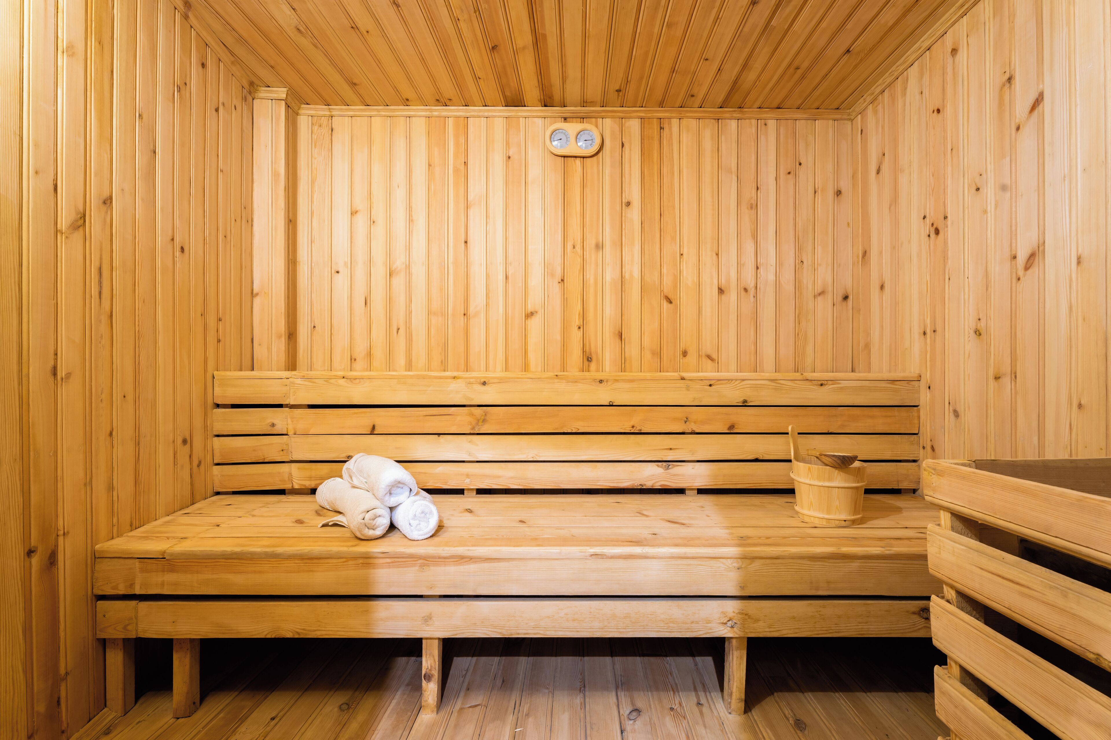A wooden sauna with benches, a bucket, and towels.