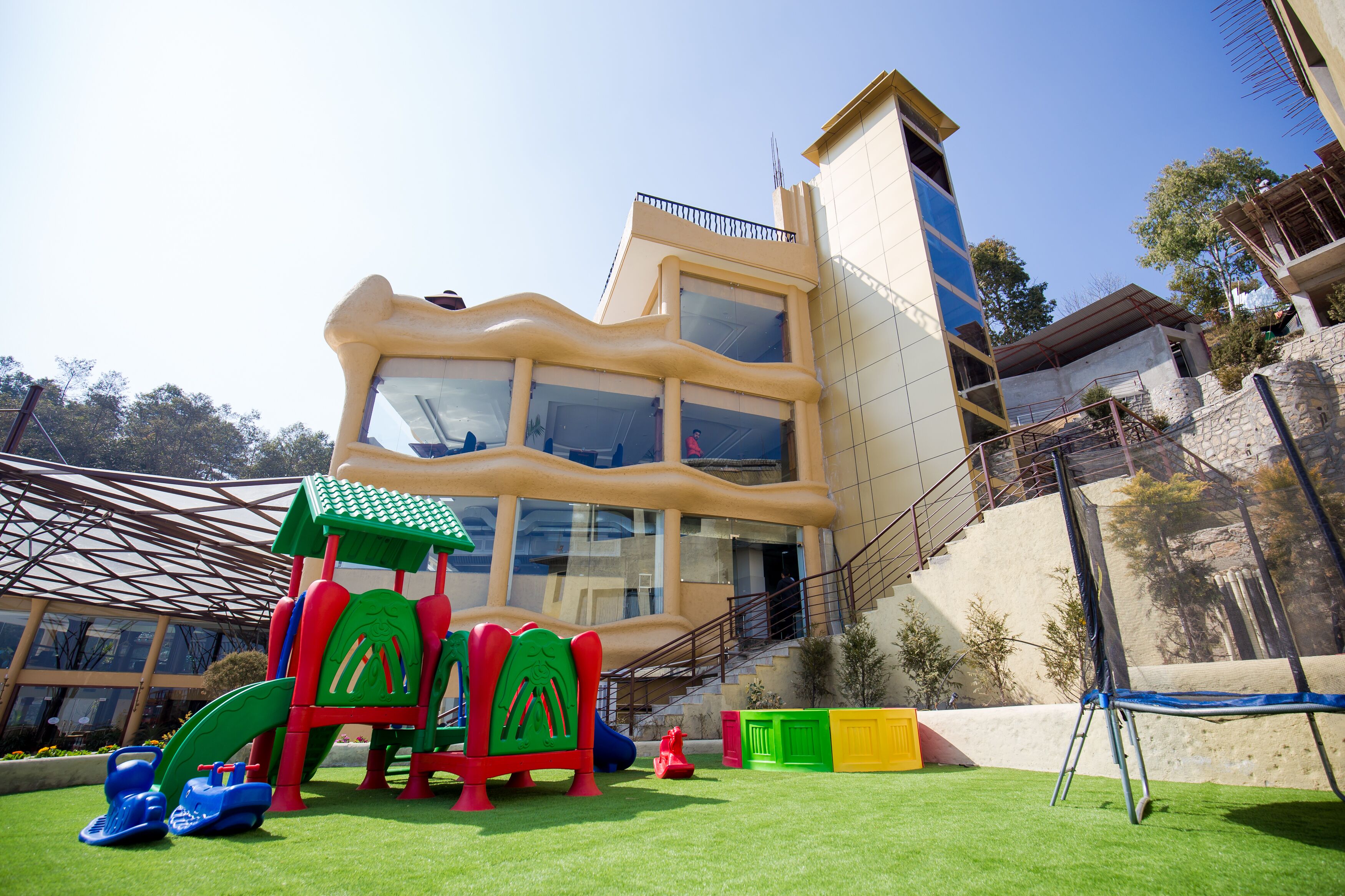 Un parque infantil con toboganes y estructuras para escalar, un edificio con múltiples ventanas y balcones, y un cielo despejado.