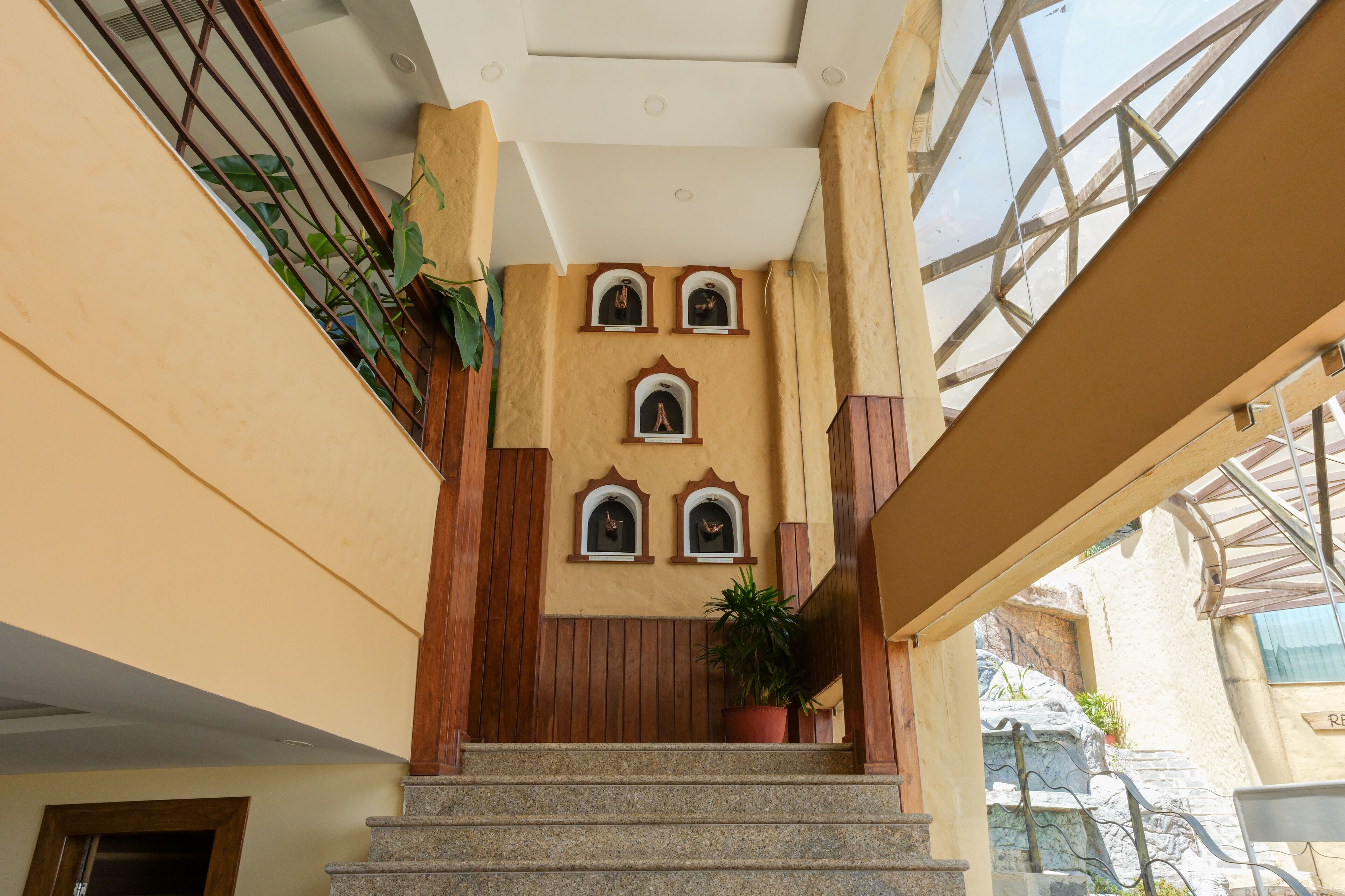 A staircase with a wooden handrail, potted plants, and decorative niches on the wall.