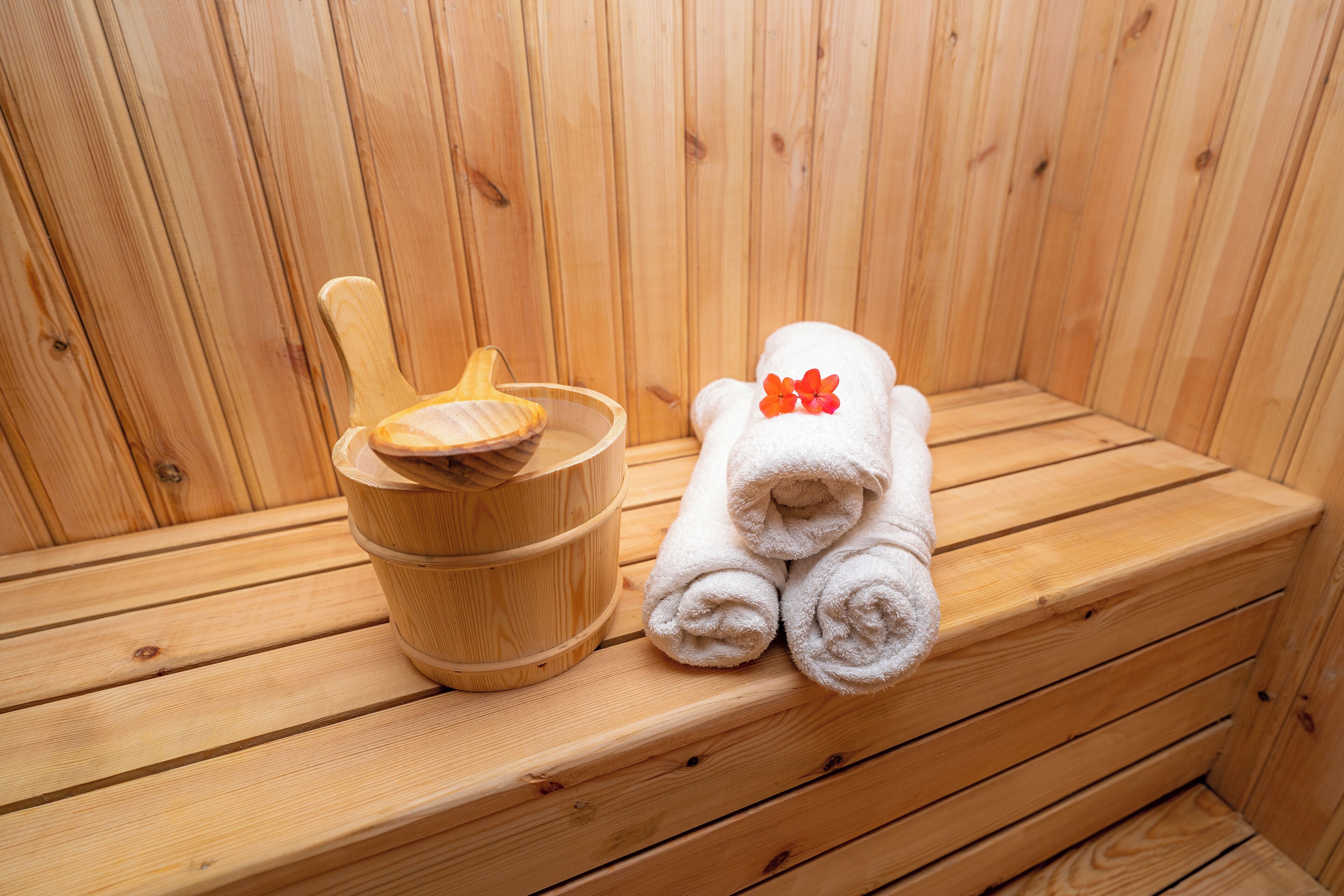 Un banc en bois pour sauna, accompagné d’un seau en bois et de serviettes enroulées.
