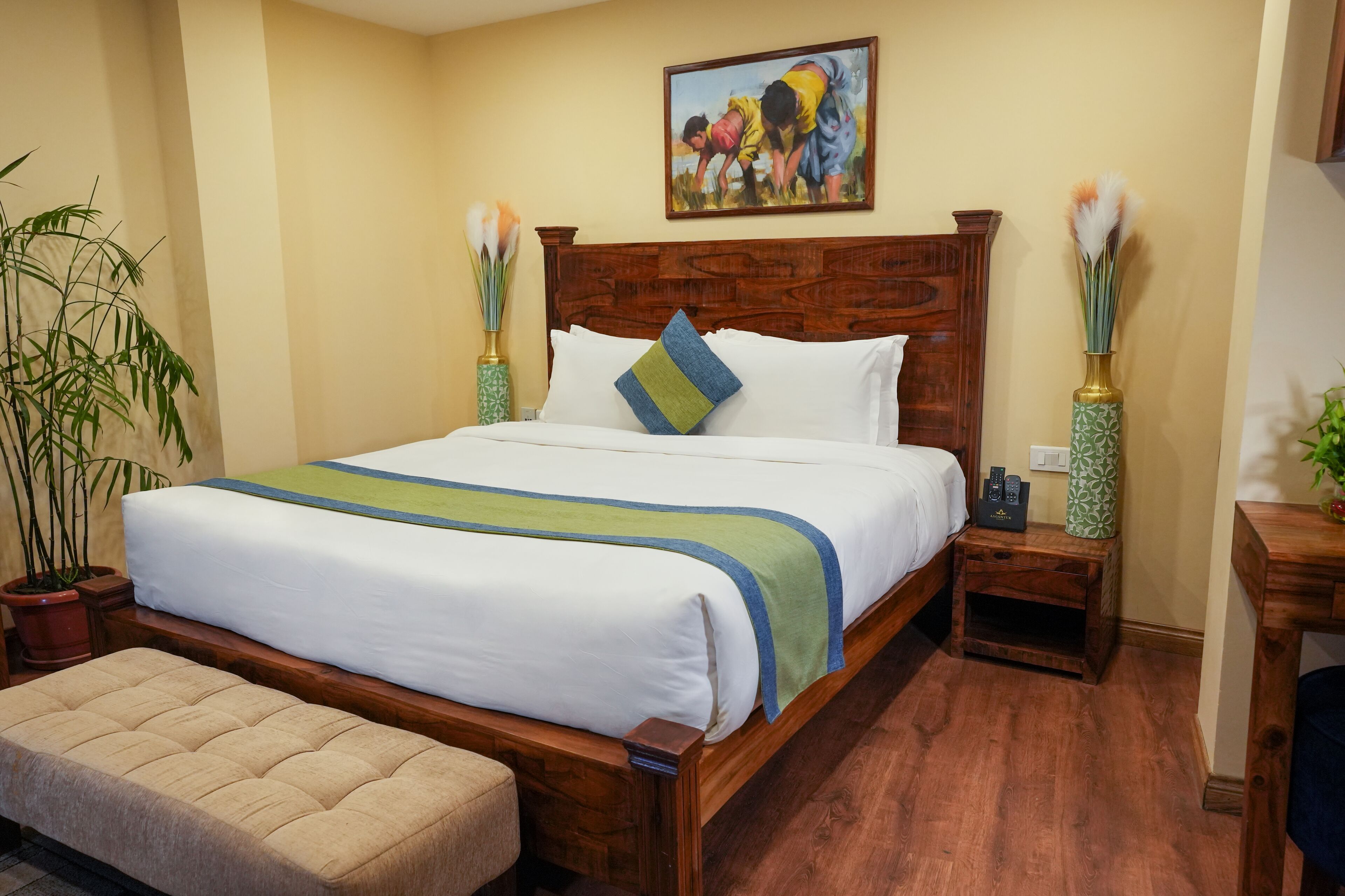A neatly made bed with a wooden headboard, a bedside table with a vase, and a painting on the wall.