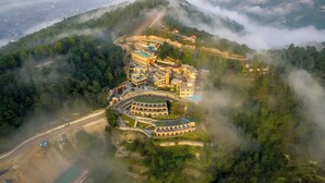 An aerial view of a hotel complex surrounded by lush greenery and mist-covered mountains. - Aagantuk Resort (Dhulikhel)