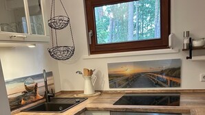 A compact kitchen with a sink, stove, oven, and a window with a view of trees.