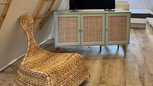 A cozy attic room with a television on a cabinet, a wicker chair, and wooden ladders.