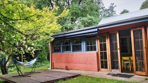 A house with a red exterior, large windows, and a wooden deck. - Redruth - 2 bedroom cottage situated in wandiligong (WANDILIGONG)