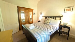A bedroom with a bed, a nightstand, a lamp, a wooden wardrobe, and a framed picture on the wall. - Redruth - 2 bedroom cottage situated in wandiligong (WANDILIGONG)