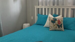 Un lit avec une couvre-lit de couleur turquoise, une tête de lit blanche et des coussins décoratifs, dont un orné d’un motif de papillon.