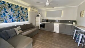 Une cuisine moderne équipée d’un four encastré, d’un micro-ondes et d’un lave-vaisselle, ainsi qu’un canapé gris avec des coussins et un ventilateur de plafond.