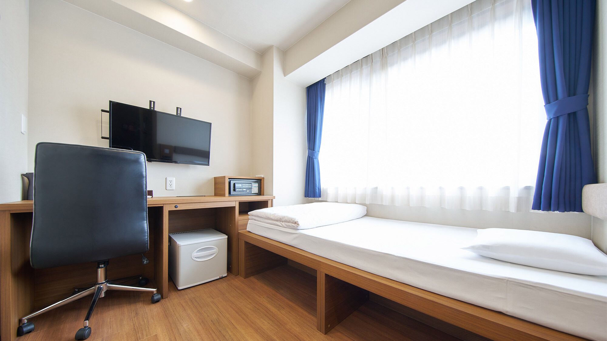 A hotel room with a bed, a desk with a computer, a chair, and a TV.