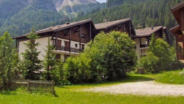 Ein traditionelles Chalet mit geneigtem Dach, Holzbalkonen und Blick auf eine Berglandschaft.