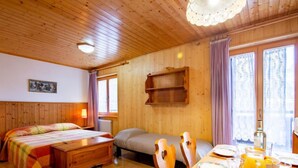 Ein Zimmer in einer Holzhütte mit einem Bett, einem Sofa, einem Frühstückstisch und einem Fenster mit Vorhängen.