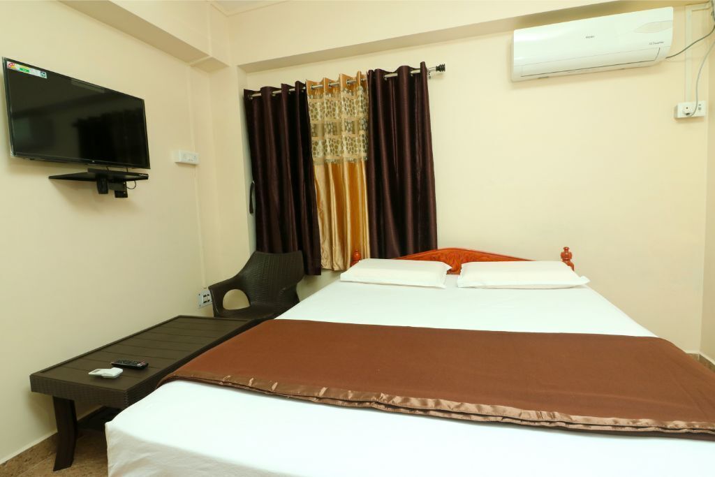 A hotel room with a bed, a TV mounted on the wall, a desk, and a chair.