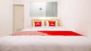 Une chambre d’hôtel avec un lit, deux oreillers rouges portant la marque « OYO », un grand miroir au-dessus du lit et une porte blanche.