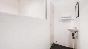 Une petite salle de bain blanche, avec un lavabo blanc, un porte-serviettes et une porte.