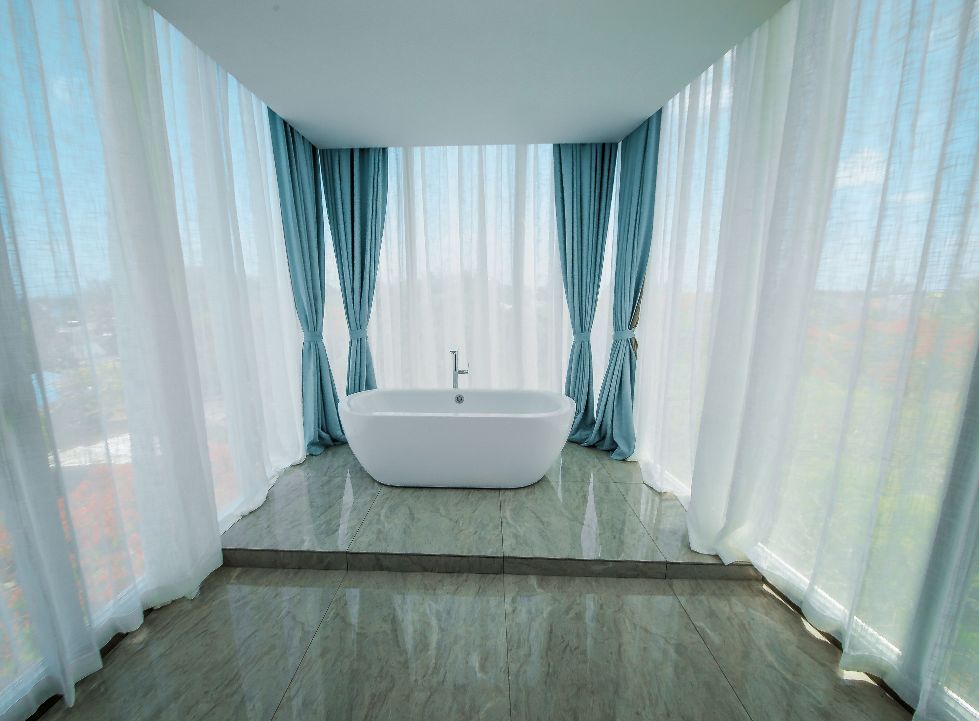 Une salle de bain moderne avec une baignoire sur pieds, de grandes fenêtres ornées de rideaux légers et un sol en marbre.