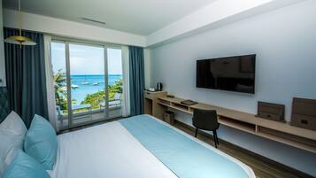Een hotelkamer met een groot bed, een bureau, een stoel, een televisie en uitzicht op de oceaan.