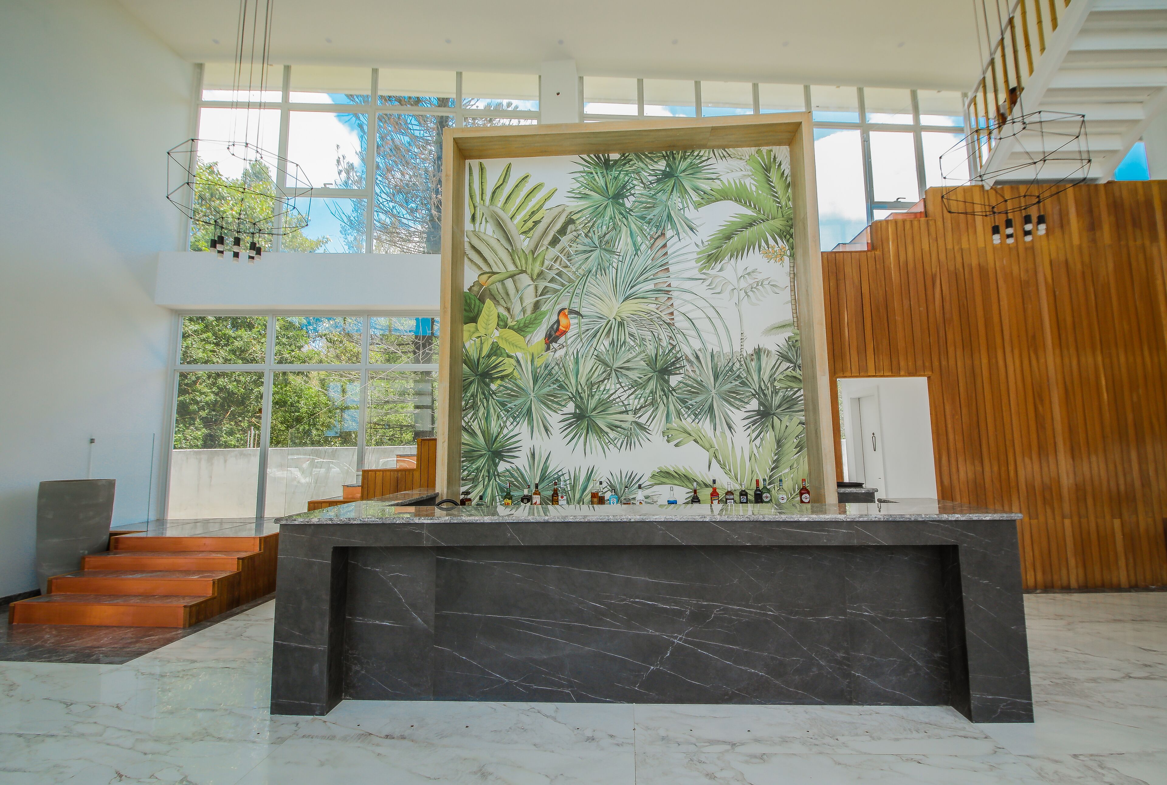 Un intérieur moderne avec un comptoir en marbre, une fresque murale aux motifs tropicaux et un escalier menant à un étage supérieur en bois.