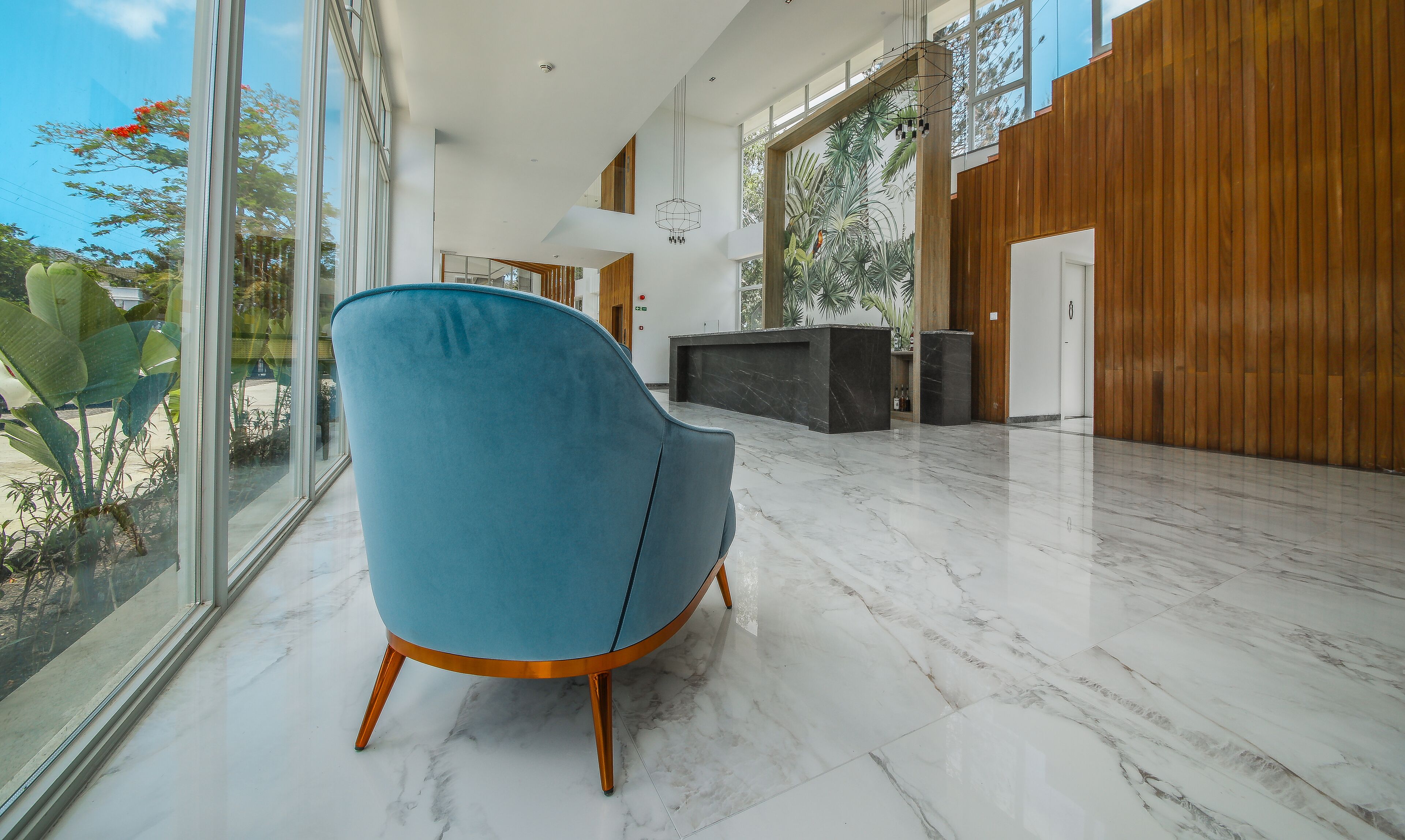 A modern interior with a blue chair, marble flooring, and large windows.