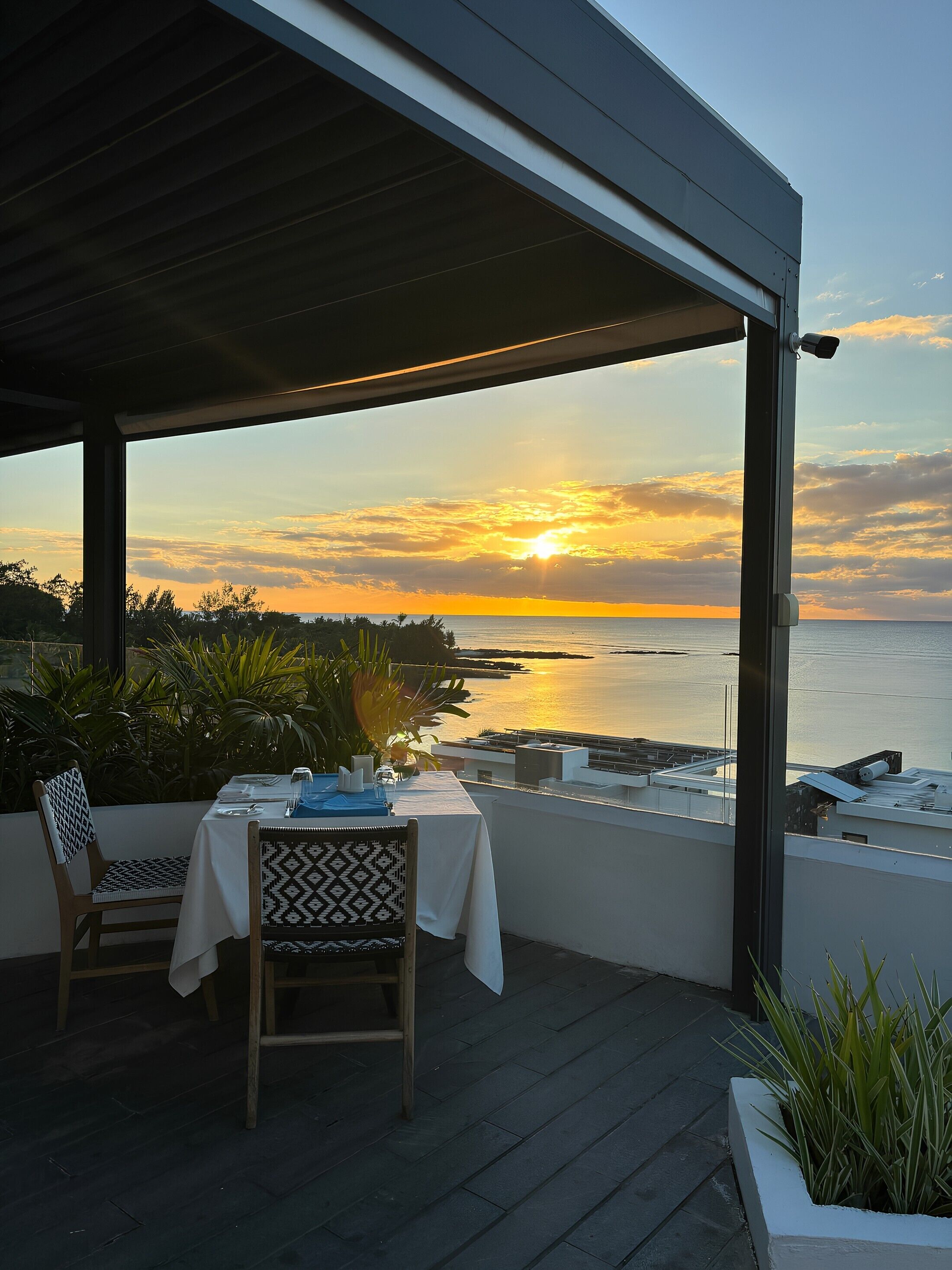 A table set for two on a balcony overlooking a sunset over the sea.