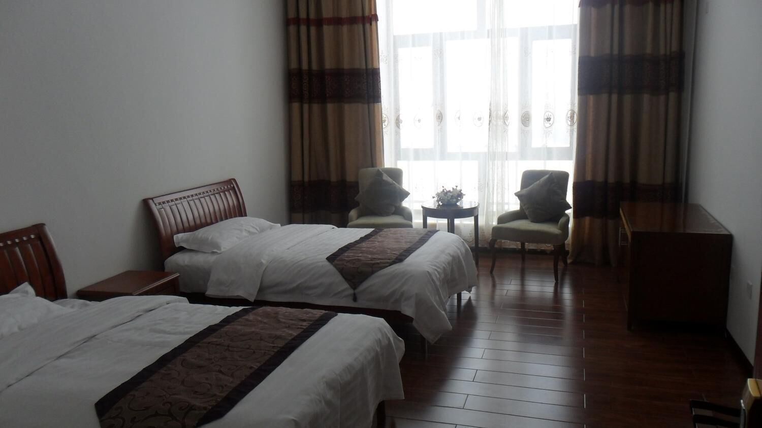 Een hotelkamer met twee bedden, een bureau, twee stoelen en een raam met gordijnen.