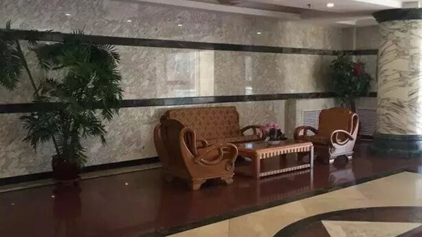 A lobby with a marble floor, two wooden armchairs, a small table, and a potted plant.