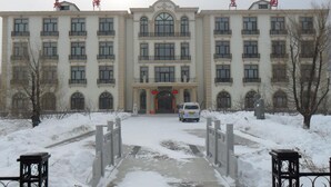 A large, multi-story building with a symmetrical facade, featuring a central entrance with a red archway and a statue.