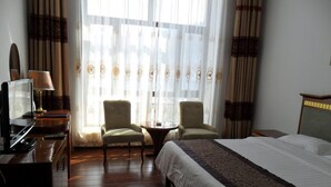 A hotel room with a bed, two armchairs, a desk with a lamp, and a television.