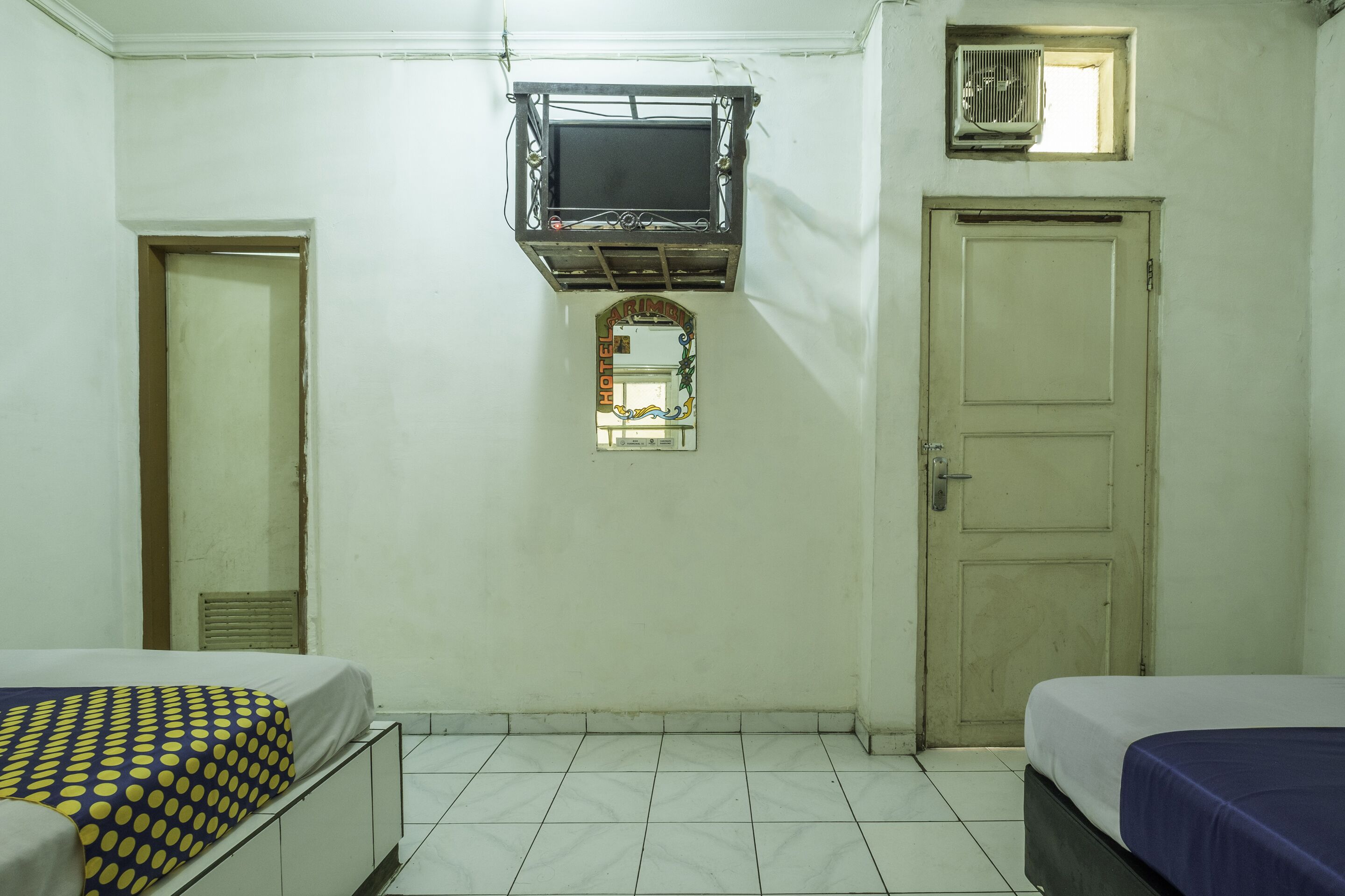 Une chambre d’hôtel avec deux lits, un téléviseur fixé au mur, une petite fenêtre et une porte.