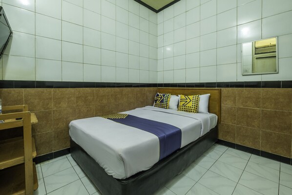 A hotel room with a bed, a wooden chair, and a mirror on the wall.