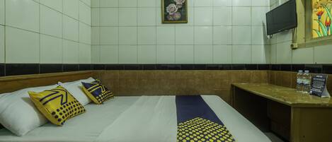 Una habitación de hotel con cama, almohadas, mesita de noche, televisor y un cuadro en la pared.