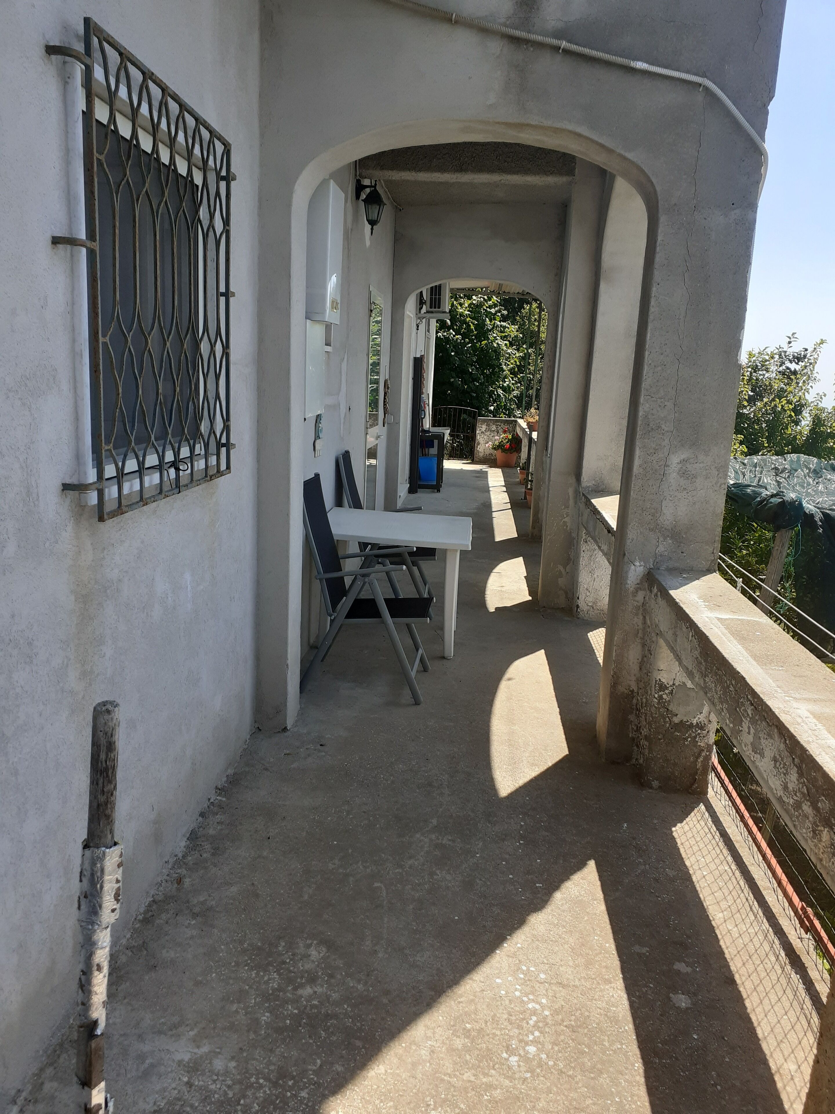 An outdoor patio area with a concrete floor, a metal railing, and a view of a garden.